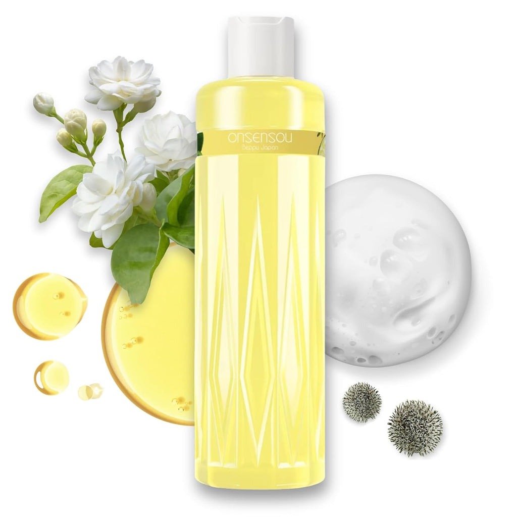 A bottle of Onsensou cleansing liquid with pale yellow liquid inside, surrounded by white flowers, green leaves, a round of creamy white foam, and small green seed pods on a white background.